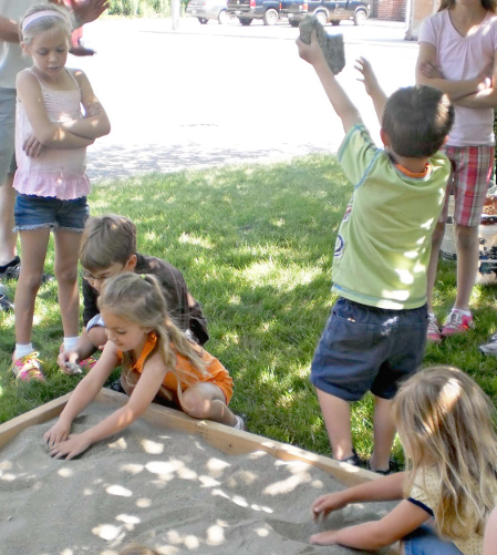 [photo of children playing in and around a sandbox]
