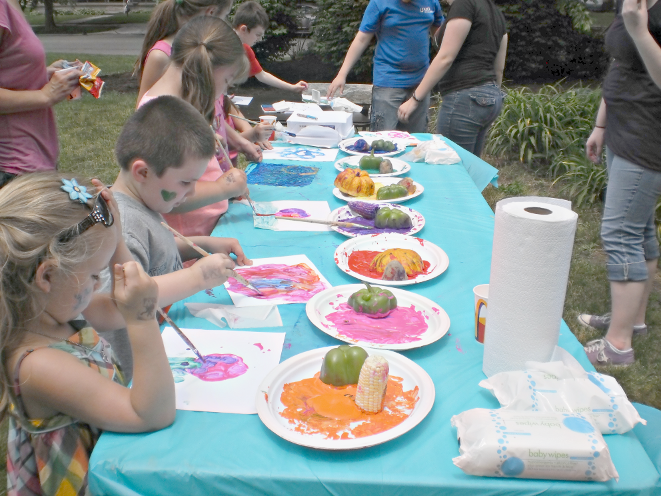 [photo of six children painting at a table]