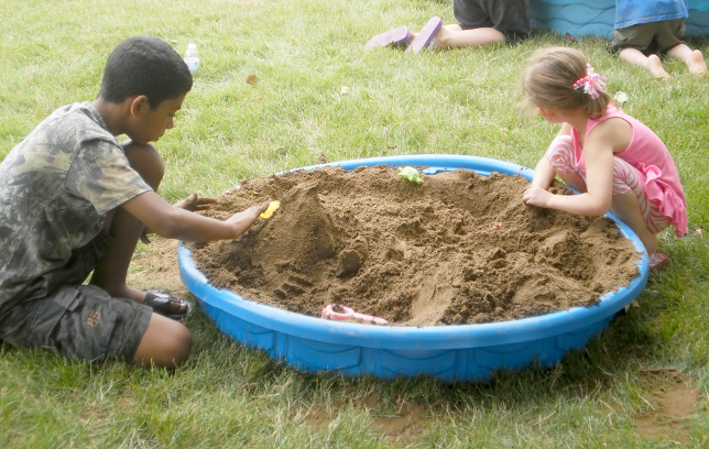 [photo of two children playing in a sandbox]