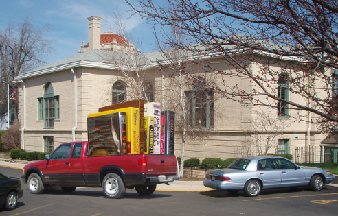 A red pickup truck with 7 comically huge books sitting in its bed.